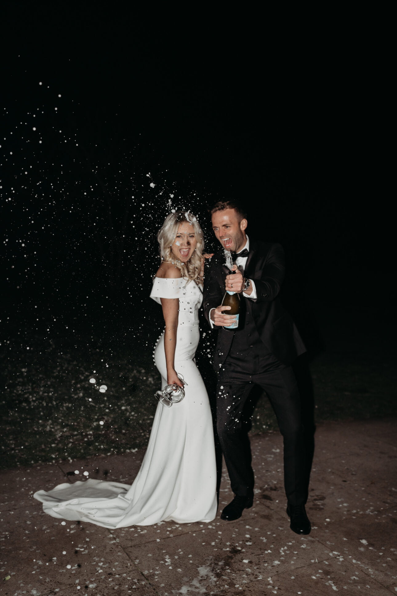 Bride and groom spraying champagne using flash photography